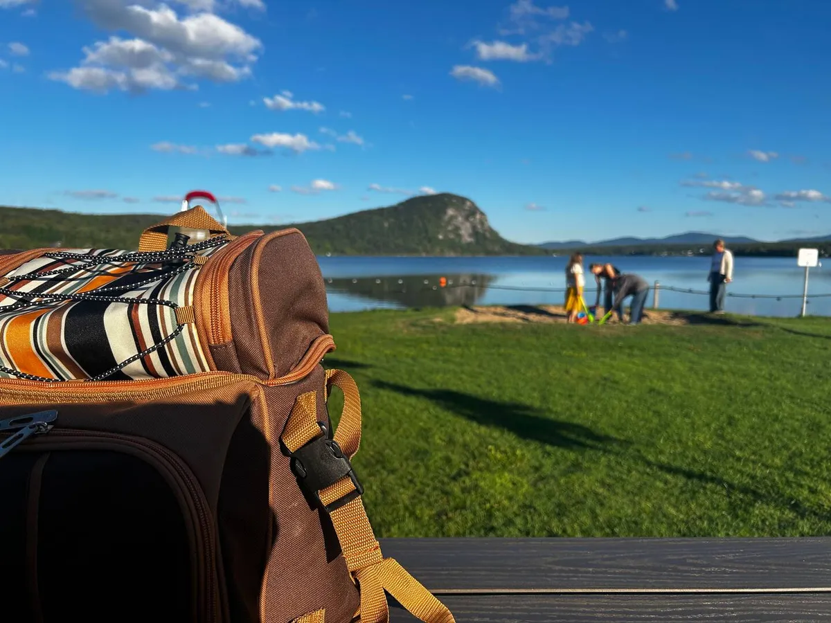 A packed picnic backpack on the grass at Lac Lyster, mountains across the water